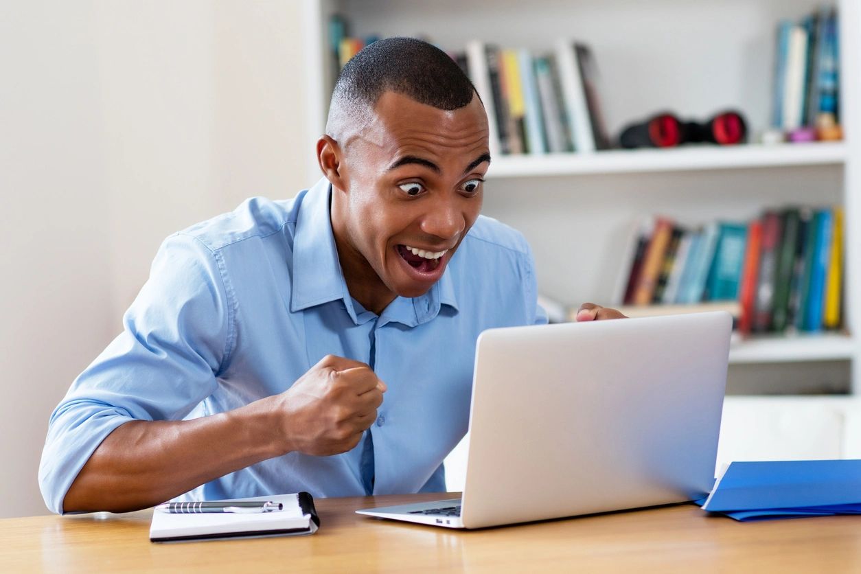 A man sitting at a table with his mouth open looking at the screen of a laptop.